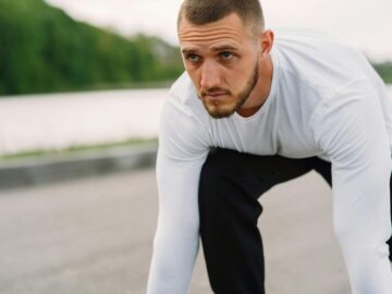 Athletic man in sportswear on a starting line, ready for a sprint workout outdoors.