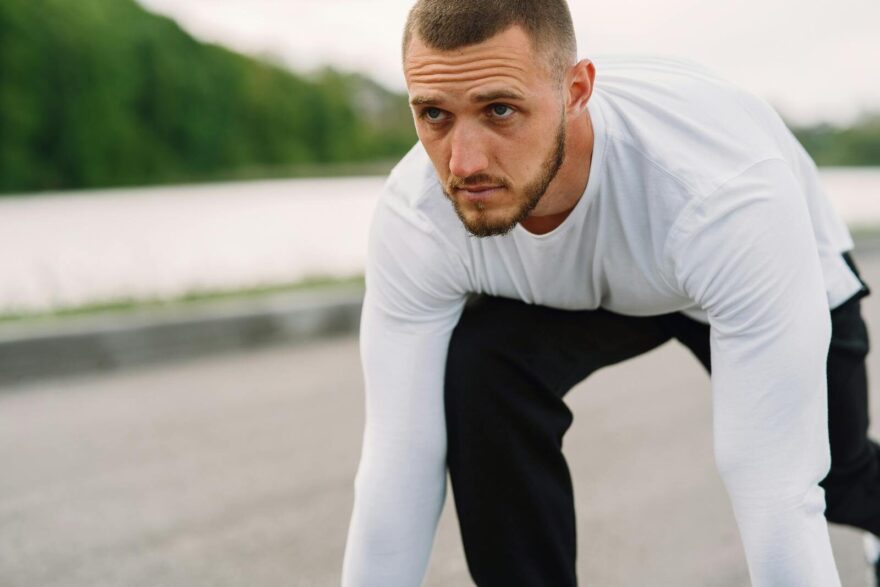 Løbeskader Athletic man in sportswear on a starting line, ready for a sprint workout outdoors.